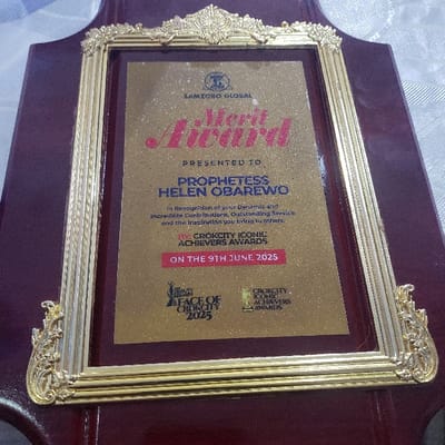 The image shows a "Merit Award" presented to Prophetess Helen Obarewo by Crokcity Iconic Achievers Awards on June 9th, 2025. The award recognizes her dynamic and incredible contributions, outstanding service, and inspiration to others. It features the "Face of Crokcity 2025" logo and the Samzoro Global logo. The award is displayed on a framed wooden plaque with a gold border.