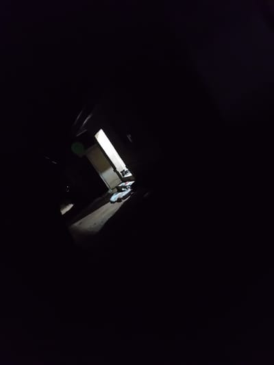 The image depicts a dark, possibly abandoned, interior space. A doorway is visible, illuminated from beyond, suggesting a passage to another area. In the foreground, there are several objects lying on the ground, appearing to be fabric or possibly discarded clothing. The overall impression is one of neglect and darkness. No specific details about the location in Barakin Angundi, Nigeria are provided by the visual information in the image itself.