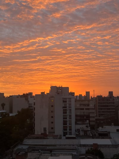 The image shows a cityscape in Cordoba, Argentina, at sunset or sunrise. The sky is filled with mammatus clouds, which appear orange-colored due to the sunlight. Tall buildings dominate the right side of the frame. The structures feature a mix of architectural styles and varying heights.