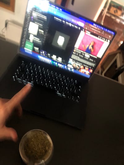 A laptop displaying a video is positioned on a dark surface. A finger is poised above the keyboard. A small, clear container filled with a green substance rests on the right side of the keyboard. The location is not identifiable as Beccar, Argentina from the provided image.