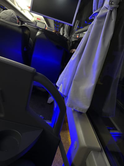The image shows the interior of a bus or similar vehicle, possibly traveling in Velika Plana Municipality, Serbia. Notable features include a pulled-back curtain, passenger seats, a small display screen, and overhead compartments. The lighting scheme includes blue accent lights, which highlight various parts of the interior. The general impression is of a modern, possibly luxury, bus interior.