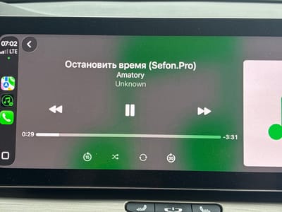 The image shows a close-up of a car's infotainment screen displaying a music player interface. The screen shows the song title "Остановить время (Sefon.Pro)" and the artist "Amatory" and "Unknown". The playback progress bar indicates the song is at 0:29 into the track, with a total remaining time of -3:31, suggesting the song has a total duration of approximately 4 minutes.
Visible icons include playback controls (rewind, pause, fast forward), shuffle, repeat, and a 15-second skip forward button. There are also icons for a phone call and app access on the left side of the screen. The time displayed at the top left is 07:02, and "LTE" indicates a cellular connection. The background of the music player is a gradient of dark gray to green. The overall setting appears to be inside a vehicle, likely during daylight hours given the brightness of the screen and the "07:02" time. No people are visible in the image. The context provided indicates the image was taken in Гаранскі сельскі Савет, Belarus.