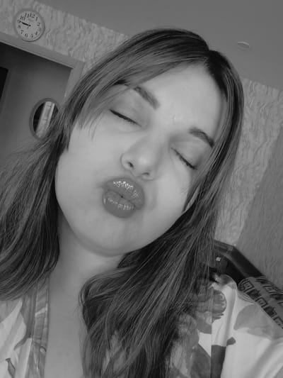 A grayscale image depicts a woman lying down, with her eyes closed and lips pursed. The background includes a clock on the wall showing 10:07, a ceiling light fixture, and a floral patterned bedspread. Location: Амзя, Russia.