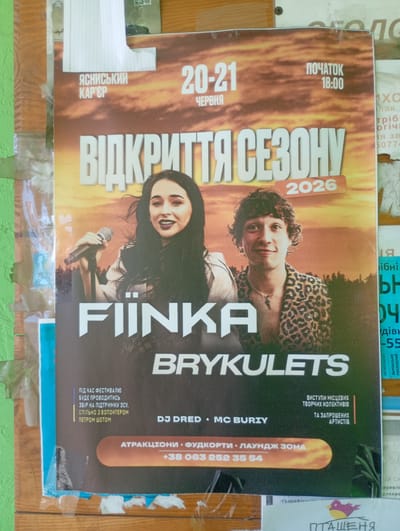 The image displays a poster for an event titled "ВІДКРИТТЯ СЕЗОНУ 2026" (Season Opening 2026) taking place on "ЧЕРВНЯ" (June) 20-21. The poster features two individuals: a woman singing into a microphone and a man wearing a leopard-print jacket. Text on the poster includes "ЯСНIСЬКИЙ КАР'ЄР" (Yasnyska Career), "ПОЧАТОК 18:00" (Start 18:00), "FIINКА BRYKULETS", "DJ DRED MC BURIY", "ВИСТУПИ МІСЦЕВИХ ТВОРЧИХ КОЛЕКТИВІВ ТА ЗАПРОШЕНИХ АРТИСТІВ" (Performances by local creative collectives and invited artists), "АТРАКЦІОНИ ФУДКОРТИ ЛАУНДЖ ЗОНА" (Attractions, food courts, lounge zone), and a phone number "+38 063 252 35 54". The poster is attached to a wooden surface with various tape and paper fragments visible. The background of the poster appears to be a sunset or sunrise sky. Another partially visible poster to the right has text in Ukrainian including what looks like "Івано" and "Різдво". The overall scene suggests an outdoor or public space where posters are displayed.