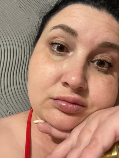 The image shows a close-up, selfie-style photograph of a woman's face. She has brown eyes and dark hair. Her face is resting on her hand, and she is looking directly at the camera. There is a textured grey background behind her. The image does not contain any information about the city of Rozkvit, Ukraine.