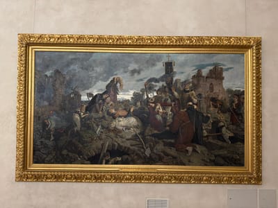 The image shows a large, ornate gold-framed oil painting depicting a chaotic and grim scene of destruction and death. The painting is hung on a textured light-colored wall. The subject matter appears to be a historical or religious event, with numerous figures in period clothing. In the foreground, there are many dead and wounded individuals lying among rubble and debris, suggesting a battle or disaster. Several figures are dressed in religious habits, including monks. Some individuals are actively engaged in rescue or aid, while others appear to be mourning or in distress.
In the background, ruined structures, possibly a church or castle, are visible against a dark, stormy sky. There are torches held by some figures, casting dramatic light and shadows. A banner with a cross is prominently displayed. The overall impression is one of tragedy, suffering, and religious devotion amidst devastation.
The text at the bottom of the painting, visible in one of the crops, reads "1899 F. STUCKELBERG 1831-1907 'Der Todten von Basel'". This identifies the artist as F. Stuckelberg and the painting's subject as "The Dead of Basel". Franz Stuckelberg (1831–1907) was a Swiss painter. This painting is indeed located in Basel, Switzerland, and it is housed in the Kunstmuseum Basel. The painting is titled "Der Tod der Bürgermeister von Basel" (The Death of the Mayors of Basel), also known as "Die Pest" (The Plague) or "Die Toten von Basel" (The Dead of Basel). It depicts the scene after the devastating plague in Basel in 1349.