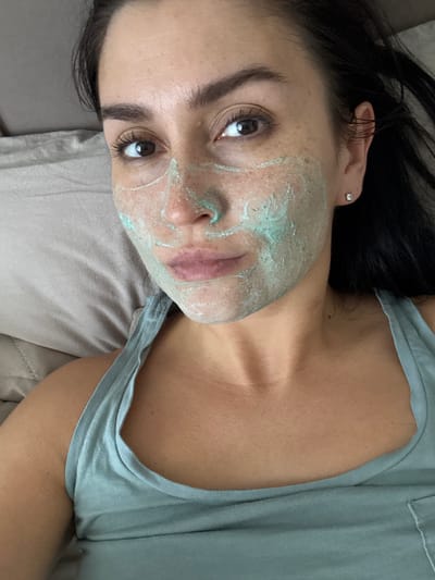 A woman with dark hair and a face mask lies on a pillow. She is wearing a light blue tank top. The environment appears to be indoors, possibly a bedroom. There is no indication of the location being the city of Нижнеяркеево, Russia.