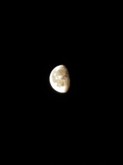 A digital photograph displays a gibbous moon, approximately two-thirds illuminated, centered against a featureless black background. The lunar surface exhibits a mottled appearance with varying shades of off-white, light beige, and brown, revealing indistinct topographical features such as craters and maria. The illumination forms a convex shape on both the right and left sides of the visible moon. No other celestial bodies or atmospheric elements are discernible. The image was recorded in Лабжанскі сельскі Савет, Belarus.