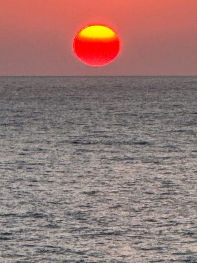 The image depicts an abstract composition with contrasting textures and colors. A half-yellow, half-red circular object appears on the left, set against a gradient background of reddish-orange. To the right, a textured, gray field dominates, resembling a rough or weathered surface with vertical patterns. A blurred line divides the colored sphere and the gray texture, creating a distinct separation between the two areas.