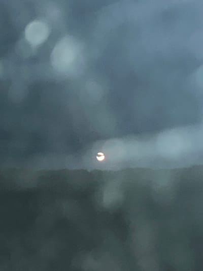 This media file is a close-up, out-of-focus photograph that appears to be taken through a pane of glass or a similar transparent surface. The dominant color palette is muted blues and grays, suggesting either a cloudy day or an indoor setting with subdued lighting.
The primary subject, though small and somewhat indistinct, is a circular object with a bright, crescent-shaped highlight. This highlight suggests a light source, possibly a reflection or a distant illuminated object. The overall blurriness of the image makes it difficult to identify the specific nature of this object or its surroundings with certainty.
There are several larger, blurred circular or oval shapes scattered throughout the frame, which are likely out-of-focus lights or reflections. A vertical, lighter-colored smudge runs down the right side of the image, which could be a streak on the surface through which the photo was taken, or part of the background.
The context provided, Tyukalinsk, Russia, does not offer specific visual cues within the image itself. The time of day and weather are indeterminate due to the blur and lack of distinct features. No people or text are visible. The image evokes a sense of subtle mystery or abstract observation, focusing on light and form rather than clear subject matter.