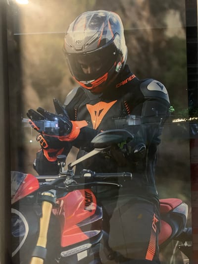 This media file shows a close-up, vertically oriented view of a motorcyclist. The subject is wearing a full set of riding gear, including a black and orange Dainese suit, a full-face AGV helmet with a clear visor, and black and orange gloves. The motorcyclist's hands are on the handlebars, with the right hand near the throttle and brake lever. The motorcycle appears to be red, with visible "DUCATI" branding on the fuel tank. The background is blurred, suggesting a fast-moving scene or a shallow depth of field. The lighting is somewhat diffused, hinting at an overcast day or early morning/late afternoon. The overall impression is one of action and performance, likely within an urban or scenic setting in Angeles, Philippines. No specific emotions are discernible due to the focus on the gear and the activity.