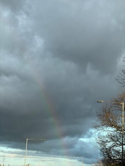 Overcast sky with a rainbow partially visible. Bare trees and streetlights are present in the frame. The location is Sandycroft, United Kingdom.