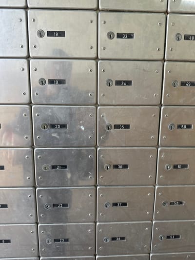 The image displays a head-on view of a grid of numerous identical silver-colored metal boxes, likely post office or security deposit boxes, located in an interior setting within the Ramat Negev Regional Council, Israel. The boxes are arranged in at least five rows and four columns. Each rectangular box features a central keyhole and a recessed black numerical display panel below it. Visible box numbers include 18, 19, 20, 21, 22, 23, 33, 34, 35, 36, 37, 38, 48, 49, 50, 51, 52, and 53. The front panel of each box is secured by four visible screws, one in each corner. The metal surfaces exhibit varying degrees of wear, including minor scuffs, scratches, and smudges, with some showing slight reflective qualities. No individuals or active interactions are present in the scene.