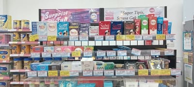 The image shows a retail display of condoms in Payakumbuh, Indonesia. Condoms from brands like Durex, Fiesta, Sutra, Okamoto, and Vivo are stacked on shelves with price tags displayed. Other products like baby formula are on shelves nearby, indicating that this is a general store or supermarket. The promotional materials include posters about "surprise fun" and offers like "buy 5 get 1 free."