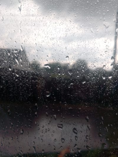 The image depicts a close-up view of a window pane covered in raindrops. The foreground is dominated by the water droplets, which vary in size and shape, some appearing as small beads and others as larger, elongated streaks. These droplets distort the view of the scene beyond the window, creating a blurred and impressionistic effect.

Through the raindrops, a somber outdoor scene is faintly visible. Dark shapes suggest buildings and trees, rendered indistinct by the water. The sky appears overcast and grey, indicating a rainy or cloudy day. The overall mood is muted and perhaps melancholic, characteristic of a rainy day.

There is no discernible activity or event taking place in the image, other than the rain itself. The time of day is difficult to pinpoint precisely due to the overcast conditions, but it appears to be daytime. The location cues are not distinct enough to provide specific information about Yessentuki, Russia, beyond the general impression of an outdoor environment. No text is visible in the image.