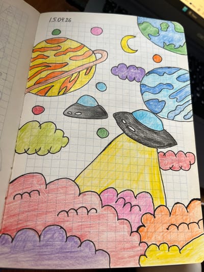 The image is a drawing on a grid-lined page, dated "15.04.26". It depicts a colorful, imaginative scene with elements of space and clouds. Several planets of various colors and designs are visible, including a ringed yellow and orange planet, two Earth-like planets (one green and blue, one light blue and blue), and smaller colored circles representing celestial bodies or moons. Two UFOs, one gray with a blue dome and another black with a blue dome, are also featured. Below the UFOs, a large yellow triangular shape, possibly representing a beam of light or a mountain, emerges from a lower section filled with large, puffy clouds in shades of red, purple, pink, and orange. The drawing is done with colored pencils and outlined in black. The background is the grid of the notebook paper. There is no indication of the city of Luque, Paraguay in this image.