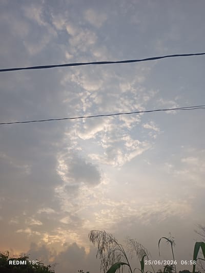 An outdoor, low-angle, full shot captures a cloudy sky at dawn, with two power lines stretching across the frame. The lower portion of the image shows the tops of tall grass and vegetation. Text overlays indicate the date and time as "25/06/2026 06:58" and the device as "REDMI 13C." The scene is set in Obada, Nigeria.