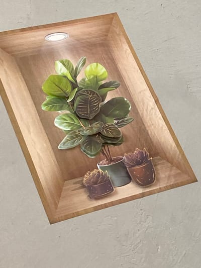 A digitally rendered image depicts a wooden display niche against a textured concrete wall. The niche is illuminated by a circular LED light source embedded in its ceiling. Inside the niche, on a wooden shelf, are three potted plants. The largest plant, positioned centrally, is a lush green specimen with large, dark-veined leaves. To its right and slightly forward is a smaller potted succulent with reddish-brown, spiky leaves. To the left and forward of the central plant is another similar succulent in a dark pot. The scene is static and appears to be a decorative arrangement, not a photograph taken in Alamüdün, Kyrgyzstan.