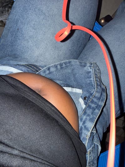 The image shows a close-up view of a person's lap, dressed in denim jeans and a black garment. A neon orange cord is draped across the denim. The scene appears to be indoors, possibly in a casual setting. The location of Abuja, Nigeria is not evident from the visual information provided in the image.