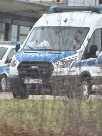A white and blue police van is parked on the street. The van has the word "POLIZEI" written in blue on the side. A license plate is visible, reading "BP-24-S/S." The van appears to be in a public area, possibly near a building. The photo is slightly grainy and the image is rotated to the side.