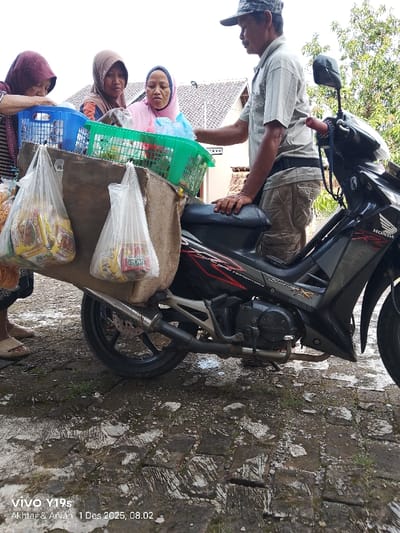 Three women and a man stand around a black Honda motorcycle loaded with goods for sale. Two blue and green plastic baskets are placed on top of the motorcycle, along with a brown sack hanging from the sides with plastic bags full of products. The man is wearing a cap, a light-colored shirt, and khaki pants. The women wear head coverings. The scene takes place on a cracked concrete or paved surface.