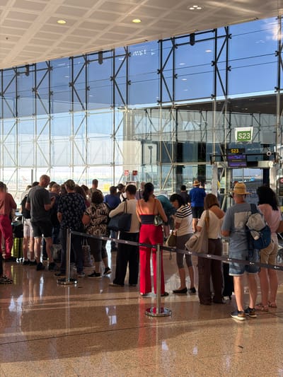 The image depicts a queue of people standing in what appears to be an airport or train station. The subjects are a diverse group of individuals, varying in age and gender, all facing the same direction, suggesting they are waiting in line for something. They are dressed in casual attire, with some carrying bags.
The setting is an indoor space with a modern architectural style, characterized by large glass panels and metal structures, reflecting natural light. The floor is a speckled, textured material, possibly granite or marble. The reflection on the floor suggests a well-lit environment. Visible in the background are signs with text, including "S23" on a green and white sign, and another digital display showing "S23," "00:00," "STUTTGART," and "EMBARQUE 07:55." This text indicates a gate number or boarding area and a departure time, confirming the airport context.
The activity taking place is clearly a queue, with people patiently waiting. There are no explicit signs of urgency or distress, suggesting a normal flow of travel. The overall mood is neutral and functional. The time of day is likely morning, given the "07:55" departure time. The weather outside, inferred from the bright reflections on the glass, appears to be sunny. The location context provided places this scene at el Prat de Llobregat, Spain, which is the location of Barcelona–El Prat Airport.