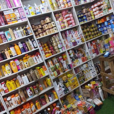Shelves overflow with diverse beauty products, predominantly skincare. Creams, lotions, and soaps dominate the selection, stacked densely and spanning multiple rows. Packaging varies from jars and bottles to boxes. A few personal care items are scattered amongst them, with a stool in the bottom-right corner holding a small device. The scene is brightly lit, showcasing a vast inventory in what seems to be a small shop.