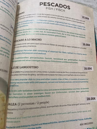The image is a close-up of a menu from a restaurant in Las Palmas de Gran Canaria, Spain. It shows a section of the menu called "Pescados" (Fish) and features four different fish dishes: Sudado, Pescado a Lo Macho, Aji De Langostino, and Jalea (2 personas / 2 people). Each dish is described in Spanish and English, and the price is listed in Euros. The background is a white tablecloth, and the menu is printed on a light-colored paper. The menu items are described in detail, including ingredients and cooking methods. The price of each dish is listed. The font is black. The text is set in two columns, with the Spanish description on the left and the English description on the right.