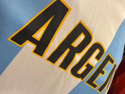 A close-up shot of fabric with the word "ARGE" printed on it, styled in black with yellow bordering. The fabric background features light blue and white stripes. The image lacks identifiable elements to connect it to Dania Beach, Florida.