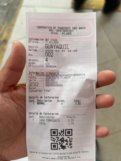 A right hand, presumably adult, holds a thermal paper bus ticket for "COOPERATIVA DE TRANSPORTE INES MARIA." The ticket, issued from the TT-MILAGRO office in Milagro, Ecuador, specifies a journey to Guayaquil, departing on March 15, 2026, at 18:00 on Bus 002, Seat 4, from Platform 016. The invoice, dated March 15, 2026, at 17:46:47, details a total cost of $1.75, which includes a $1.55 fare and a $0.20 turnstile fee. A QR code for electronic invoicing is visible at the bottom. The background is blurred, showing light, indistinct surfaces, suggesting an indoor or sheltered environment.