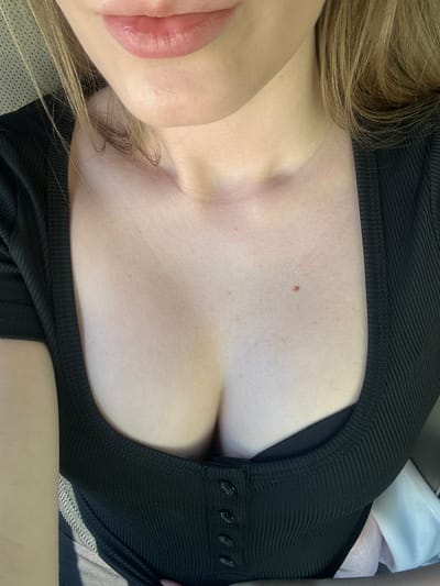 The image is a close-up, chest-level, outdoor shot of a person wearing a black, ribbed, scoop-neck top. The person has fair skin and blonde hair. The background is slightly blurred, but appears to be the interior of a vehicle, possibly with a dotted textured seat visible on the left. The lighting suggests it is daytime. The image does not provide any specific details about the city of Everett, United States of America, or any other environmental context.