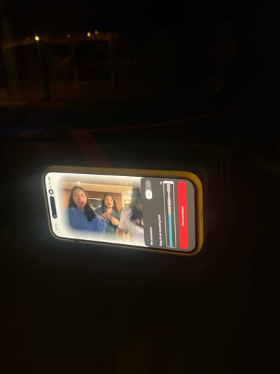 A smartphone with a yellow case is held in a dark indoor environment. The phone's screen displays a video of three people. The person in the foreground is wearing a blue shirt. The phone's screen also shows controls for setting a recording countdown. The time displayed on the phone is 20:48. The location, El Oasis Valsequillo, Mexico, cannot be determined from the image.