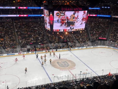 The image shows a hockey game in progress at T-Mobile Arena in Las Vegas, Nevada. The home team, the Vegas Golden Knights, are playing against a team wearing red jerseys. The scoreboard shows the Golden Knights leading 8-0 in the first period with 8:33 remaining on the clock. Fans are visible in the stands, mostly wearing Golden Knights colors. Several advertisements line the ice rink perimeter.