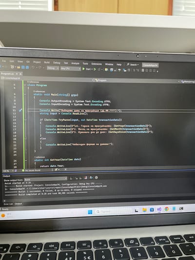 The image captures a close-up, rotated view of a laptop screen displaying a C# development environment within Visual Studio. The laptop is an HP model, indicated by the logo on the spacebar of the keyboard, which features Cyrillic characters.
The primary activity is software development, with C# code visible on the screen. The code defines a `Program` class with a `Main` method that attempts to parse a transaction date input from the user. It then calculates and displays the year, month, and days since the transaction, with error handling for invalid date formats. The console output and user prompts are in Bulgarian, including phrases like "Въведете дата на транзакция" (Enter transaction date) and "Невалиден формат на датата!" (Invalid date format!).
Notable details include the Visual Studio IDE in a dark theme, showing project "ConsoleApp34". The "Output" window confirms a successful build operation, stating "Build started at 8:28..." and "Build completed at 8:28 and took 00,506 seconds". The status bar also indicates "Ready", "18°C", and "Sunny" weather conditions. A webcam is visible on the top bezel of the screen. The Windows taskbar is partially visible at the bottom, showing icons for applications like Chrome and Visual Studio Code, and a search bar with "Търсене" (Search) in Bulgarian. The presence of Cyrillic text on the keyboard and in the code aligns with the location context of Nova Zagora, Bulgaria.
