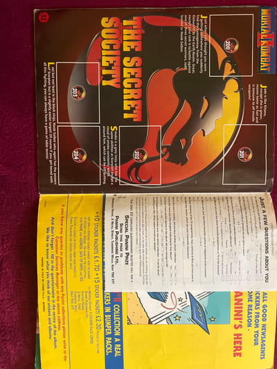The image is a scan of a page from a "Mortal Kombat" sticker album, featuring artwork related to the game's characters and lore. The page is predominantly dark red and black with yellow text.
**Key visual elements include:**
* **Title:** "THE SECRET SOCIETY" is emblazoned across the top in large, bold, yellow letters.
* **Character Art:** Stylized artwork of characters, possibly from Mortal Kombat, is integrated into the background and around the text. This includes a large, stylized mask-like design and other graphical elements.
* **Sticker Numbers:** Several circular callouts with numbers (200, 201, 202, 203, 204) are present, indicating where stickers would be placed.
* **Text Blocks:**
* A block of text in the upper right describes the "MORTAL KOMBAT" title and the "JUST A FEW QUESTIONS" section.
* A description of the "SECRET SOCIETY" is provided, mentioning characters like "Jade," "Kitana," "Scorpion," "Smoke," and "Noob Saibot."
* A section detailing how to order "STICKER PACKETS" is present at the bottom, including an address: "PANINI PUBLISHING LTD, PANTILE HOUSE, 2 NEVILL STREET, TUNBRIDGE WELLS, KENT TN2 5TT."
* A final block of text states "PRINTED IN ITALY BY PANINI S.p.A. - MODENA."
* A prominent yellow section on the right reads "ALL GOOD NEWSAGENTS STICKERS FROM YOUR ANINI'S HERE IN BUMPER PACKS."
The image is a flat, two-dimensional representation of printed material. There are no people, animals, or active events depicted. The environment is not a specific real-world location but rather a page from a publication. The mention of "Кенен Әзірбаев ауылы, Kazakhstan" is not supported by any visual evidence within the image itself; this information appears to be external context provided to the AI.