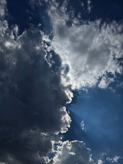 This media file depicts a dramatic sky with a mix of dark, heavy clouds and bright, sunlit ones. The sun is partially obscured, casting rays of light that pierce through the clouds, creating a sense of depth and intensity. The sky transitions from a deep blue in the upper right portion to a more muted, overcast appearance as it moves towards the left and bottom of the frame. The clouds are varied in texture and density, with some appearing fluffy and white at the edges where they catch the sunlight, while others are dark gray and ominous. This contrast between light and shadow suggests a dynamic weather system, possibly a storm approaching or breaking. The scene evokes a sense of awe and perhaps a touch of foreboding due to the strong contrast and dramatic lighting. There is no visible text. Given the location context of Yevpatoriya, Ukraine, this sky could be representative of coastal weather patterns. The time of day is difficult to determine precisely due to the cloud cover, but the angle of the sun's rays suggests it is not midday.