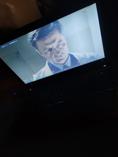 The image shows a close-up of a laptop screen displaying a paused video of a man in a white coat, likely a doctor or scientist, with a serious expression. The video player controls are visible at the bottom of the screen, indicating the video is at timestamp 35:12 out of 44:26. The laptop is placed on a dark surface, and a portion of its keyboard is visible. The background of the video appears to be a brightly lit, sterile room. The overall scene is dimly lit, suggesting the image was taken in a dark environment, possibly at night or in a room with the lights off. The location of Tsentalnyy-Kospashskiy, Russia is not discernible from the image itself.