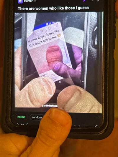 This media file is a close-up photograph of a person holding a smartphone, which is displaying an image with text. The photograph is taken from a slightly elevated angle.
The subjects in the foreground are a human hand, with the thumb and forefinger visible, holding the phone. The smartphone itself is black with a protective case. The screen of the phone is the primary focus of the image.
On the phone screen, a meme is displayed. The meme features a close-up image of fingers and a piece of paper with text. The visible text on the phone screen reads: "Humor Th", "There are women who like those i guess", "If your finger looks like this don't talk to me", and "y to MrTechnical". Below the meme, there are buttons labeled "meme", "random", and some navigational icons.
The background of the original image is blurred but appears to be an indoor setting with a textured surface, possibly a car interior or a similar environment.
The activity taking place is the viewing of a meme on a smartphone. There are no specific cues about the time of day, weather, or a precise location beyond what is implied by the screen content. The overall tone of the meme appears to be humorous, as indicated by the "Humor" label.