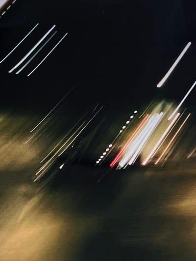 The image captures a blurred, abstract scene of light trails, likely from vehicle headlights and taillights at night. The dark background suggests an outdoor urban environment. The light trails are elongated and diagonal, indicating movement. There are streaks of white, red, and yellow light, consistent with car lights. The lower portion of the image shows a yellowish, diffused light, which could be streetlights or reflections on a wet surface. The overall impression is one of motion blur in a city setting. There is no discernible detail to indicate the specific location in Genemuiden, Netherlands.