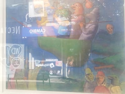 A painting hangs in front of a window displaying signs for "Cambio" (exchange) and "Exchange Holyloch." The painting depicts a surreal scene of anthropomorphic figures in a boat, accompanied by a skull. Below them, a second group of figures with pointed hats is visible. The reflections on the window obscure parts of the artwork, creating a layered visual effect.