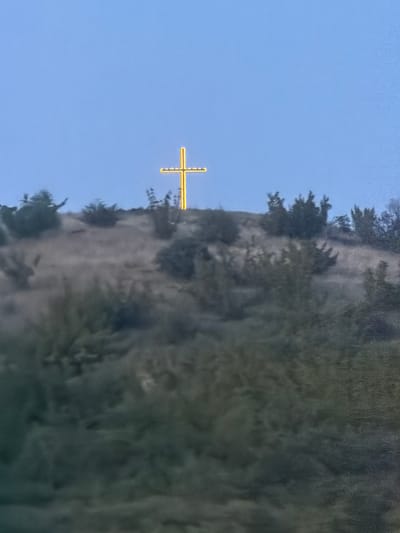 A landscape image shows a mountainside with trees and vegetation against a clear blue sky. There is a yellow crosshair or targeting reticle visible in the center of the sky. There is no city in the image and no location in Mitino, Bulgaria, can be confirmed based on the visual information provided.