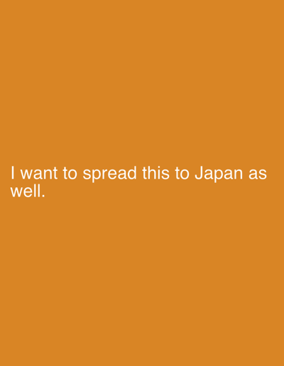 The image displays a solid orange background. In the lower-left portion, white sans-serif text is centrally aligned, stating: "I want to spread this to Japan as well." No other visual elements, figures, or objects are present.
**Location:** The image provides no visual or textual information to identify a specific location, including within the city of Toyota, Japan. The text references "Japan" as a general geographical target, but offers no localized context.
**People:** No individuals are depicted.
**Subjects:** The primary subject is the white text message displayed against the orange background.
**Objects:** No physical objects are discernible.
**Actions:** No actions or events are shown.
**Interactions:** No interactions between subjects or objects are depicted.
**Environment:** The environment is a uniform, solid orange color field, indicating a digital graphic or a single-color screen display. There are no visible topographical, architectural, or natural features.
