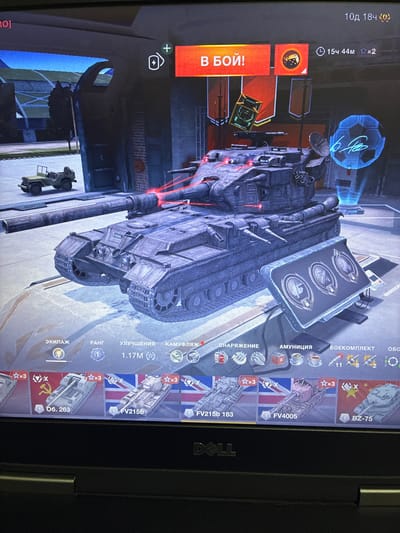 The image shows a screenshot of a video game interface, likely a tank battle game. The central focus is a 3D rendered image of a tank. Various game-related elements are visible, including: "В БОЙ!" (In Battle!) button, timer, player stats, and a selection of tanks at the bottom of the screen. There is a small green jeep in the background on the left. The image is a photograph of a computer screen. There is no indication of the city of Melitopol, Ukraine, in this image.