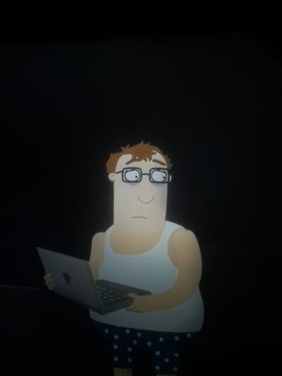 In a dark environment, an animated character is depicted. The character has light-skinned features, brown curly hair, and wears black-rimmed glasses. They are dressed in a white tank top and navy blue polka dot pajama bottoms. The character is holding a silver laptop with a partially visible apple logo. The character's facial expression appears neutral or slightly concerned. The background is entirely black, suggesting a dimly lit or nighttime setting. There is no visible indication of the city of Kuyagan, Russia, in this image.