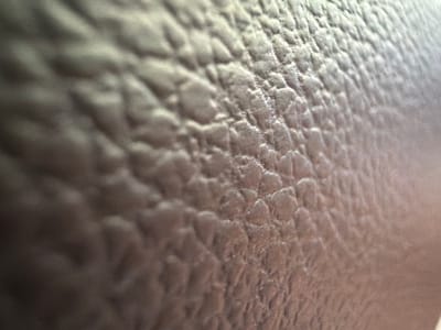 The image is a close-up, low-angle macro photograph of a textured surface that appears to be the skin of a person's arm. The skin has a matte, slightly dull finish and is characterized by visible pores and a natural, uneven texture. The lighting suggests it is an indoor environment, possibly a home, with soft illumination highlighting the contours and subtle variations in the skin's surface. There are no other discernible objects or individuals in the frame, focusing solely on the detailed texture of the skin. The location within Southlake, United States of America, is not identifiable from the visual information provided in the image.
