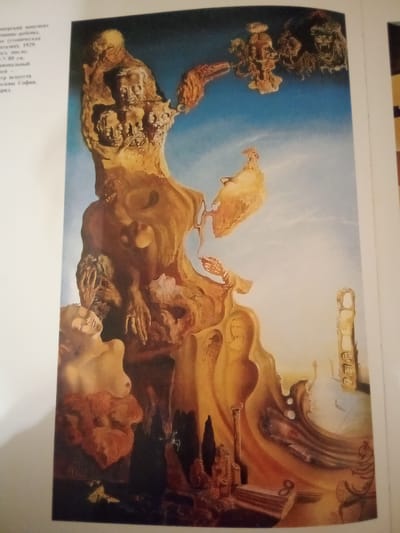 The image is a painting featuring a surreal landscape with distorted figures and architectural elements. In the foreground, a female torso is visible, with a head turned upwards and eyes closed. Behind her, a large, amorphous, golden-brown form dominates the center of the composition. This form contains multiple faces and skeletal structures embedded within it. In the upper part of the painting, several grotesque faces emerge from a cloud-like formation in a bright blue sky. The background depicts a distant, fragmented architectural ruin under a pale sky.

The provided text on the left side of the image contains information in Russian about a monument. It translates to: "Zhmerynka monument to the child (utopian fantasy), 1929. Canvas, oil. 80 X 80 cm. National Art Center, Sofia." This indicates that the painting depicts the "Zhmerynka Monument to the Child," a work by an unknown artist created in 1929, executed in oil on canvas, measuring 80 by 80 cm, and currently housed in the National Art Center in Sofia. The text also lists "Zhmerynka, Ukraine" as a location. However, it's important to note that this is a surreal painting, and it is unlikely to be a direct, realistic depiction of a specific location in Zhmerynka. Instead, it is a symbolic or imagined representation associated with the city.