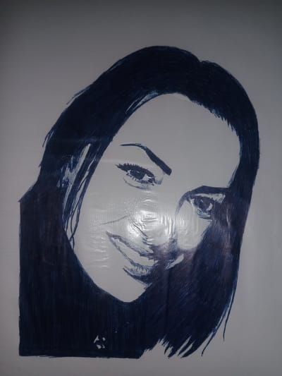 This is a portrait drawing of a woman's face, executed in dark blue marker on a white surface. The drawing depicts the woman from the shoulders up, with her head tilted slightly to her right. Her hair is dark and falls around her face and shoulders. Her eyes are open, with visible eyelashes, and she has a subtle smile. The drawing has a somewhat sketch-like quality, with visible strokes and shading. The white surface appears to have a subtle texture, possibly from a canvas or textured paper, and there are visible reflections on its surface, suggesting it might be laminated or covered with a protective plastic layer. There are no discernible elements in the image that would indicate a specific location within the city of Gulbag, Uzbekistan.