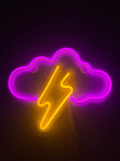 The image shows a neon sign depicting a purple cloud with a yellow lightning bolt inside. The sign is mounted on a dark, textured wall. There are no people visible in the image. The location is not specified in the image.