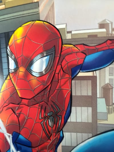The image is a close-up, comic-book style illustration of Spider-Man. He is depicted from the chest up, with his iconic red and blue suit featuring the spider emblem on his chest. His mask covers his entire head, with large, white, reflective eye lenses outlined in black. The background consists of a stylized cityscape with buildings rendered in muted tones. There is no indication of any specific location in Ödsmål, Sweden, or any other real-world place. The focus is entirely on the character and his costume.