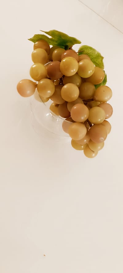A bunch of light-colored grapes, some appearing slightly translucent, are arranged in a glass bowl on a light-colored, possibly reflective surface. Green leaves are attached to the stem of the grapes, adding a touch of natural color. The overall lighting is bright, creating soft shadows. The image appears to be taken indoors, with the background being a uniform, pale color. There is no indication of the city of Winnenden, Germany, in this image.